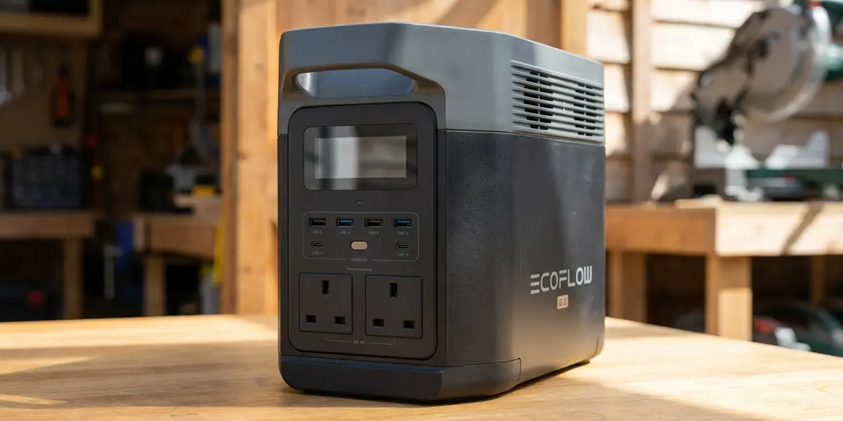 A black and grey EcoFlow Delta 2 portable power station with a digital display and dual UK AC outlets, sitting on a wooden workbench in a workshop.