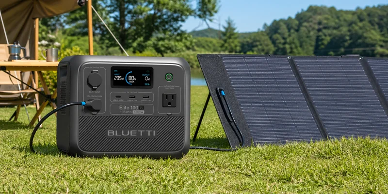 A Bluetti Elite 100 V2 portable power station connected to solar panels on grass.