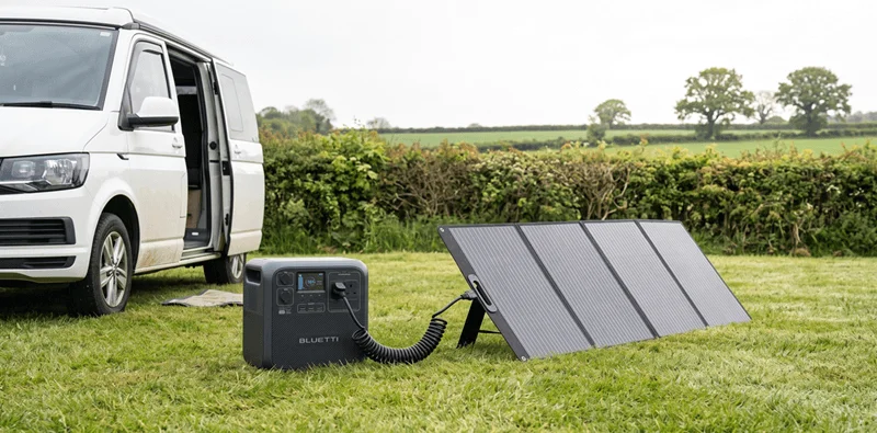 A Bluetti Elite 200 V2 portable power station connected to a solar panel beside a campervan.